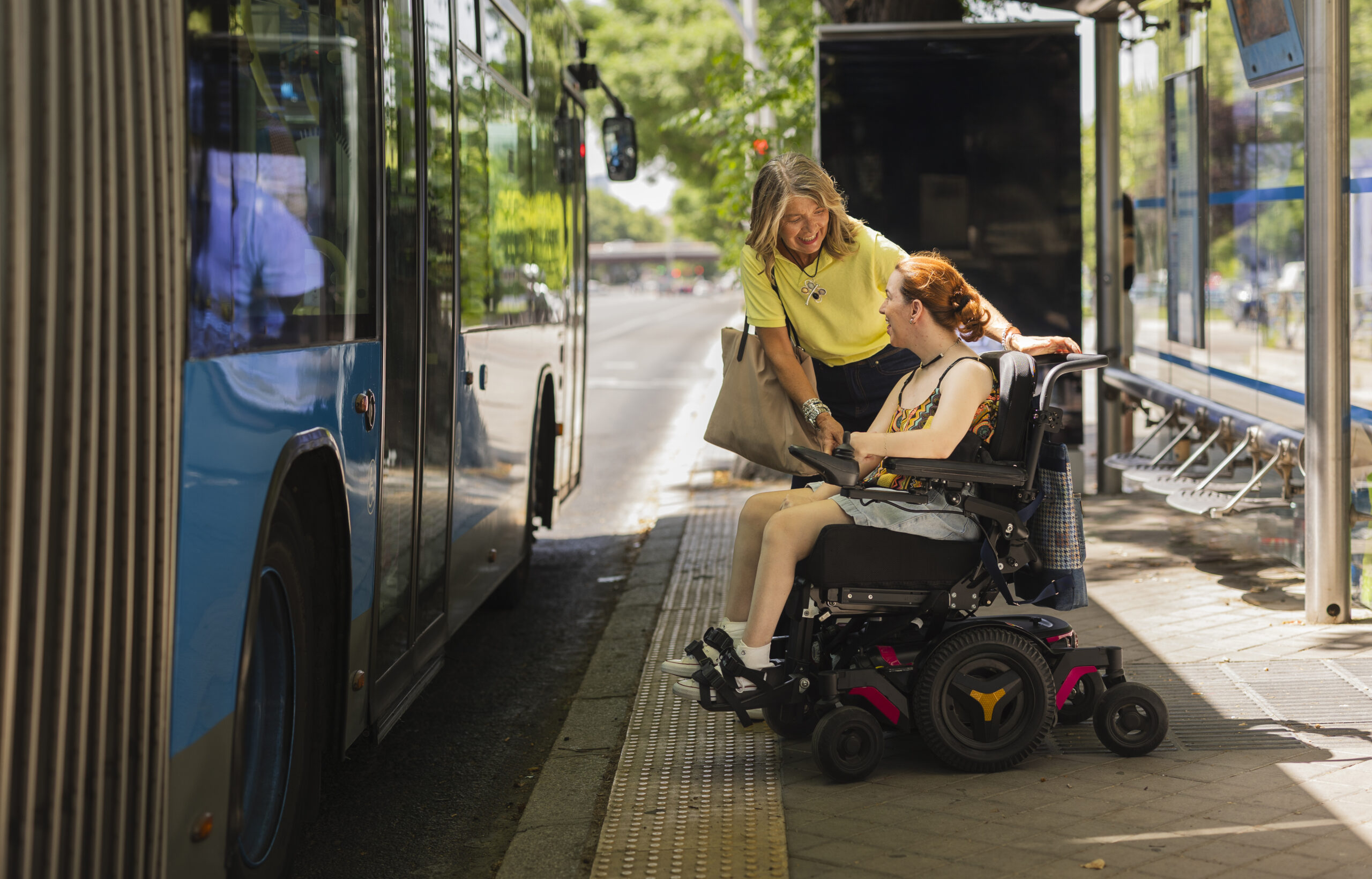 Woman helping disabled girl on wheelchair to board bus at bus stop