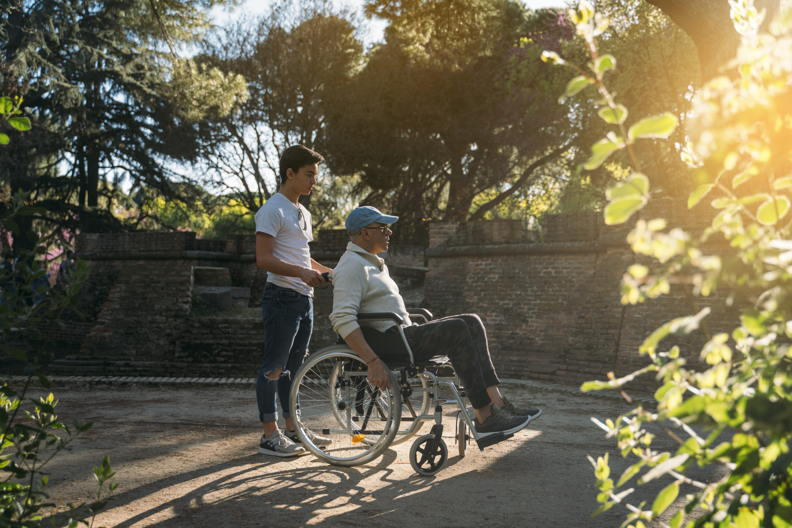 56 year old male sitting on a wheelchair and he young friend in the park
